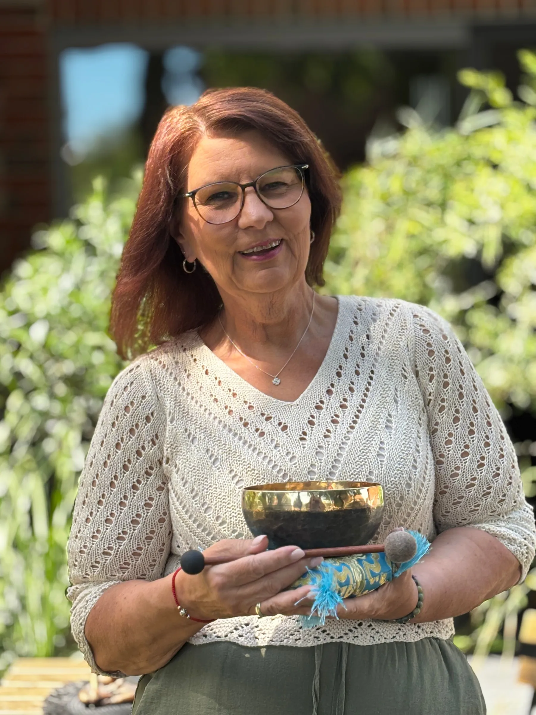 Annette Pitcher steht im Garten und hält eine goldene Klangschale mit Klöppel in den Händen