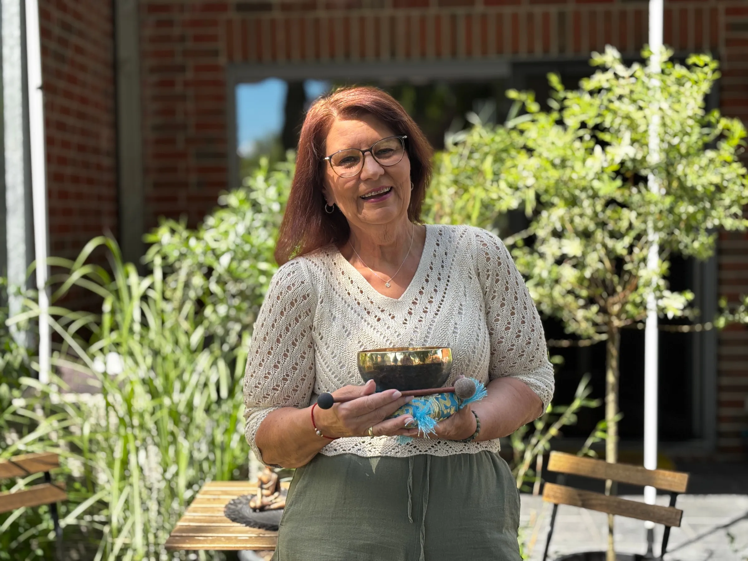 Annette Pitcher steht mit einer Klangschale in den Händen auf ihrer Terrasse