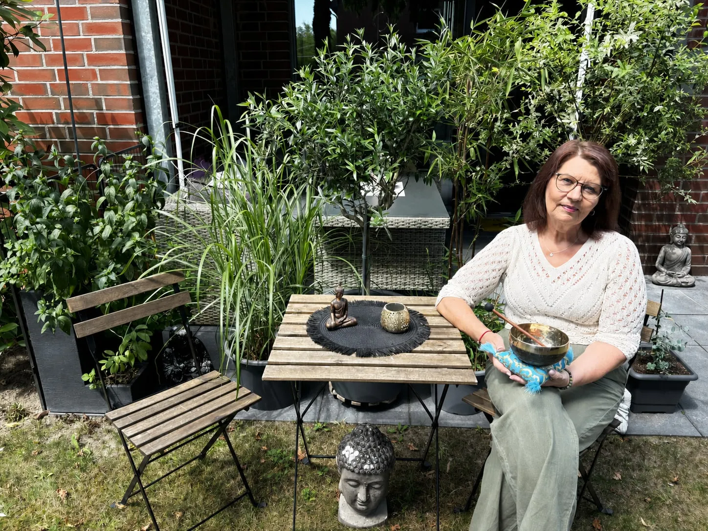 Annette Pitcher sitzt an ihrem Gartentisch, eine Klangschale in den Händen