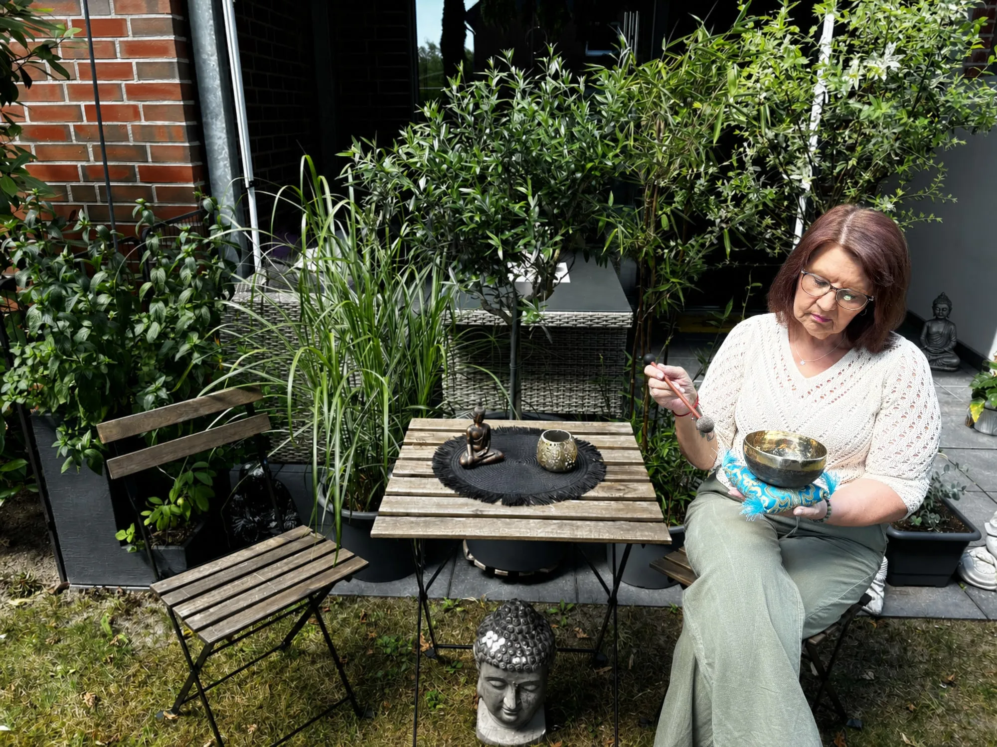 Annette Pitcher sitzt an ihrem Gartentisch, eine Klangschale in den Händen