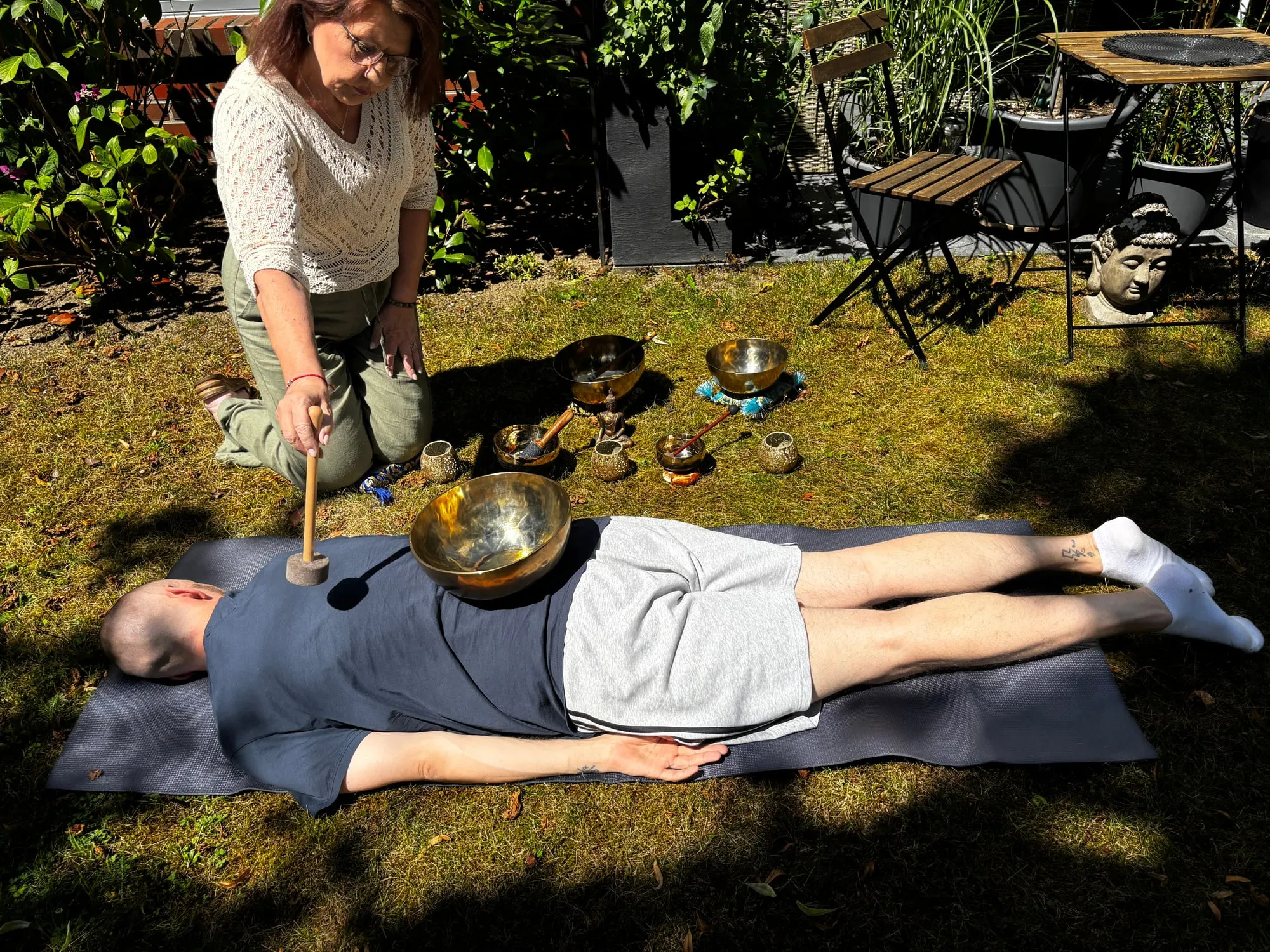 Annette Pitcher schlägt eine Klangschale an, die auf dem Oberkörper einer liegenden Person steht